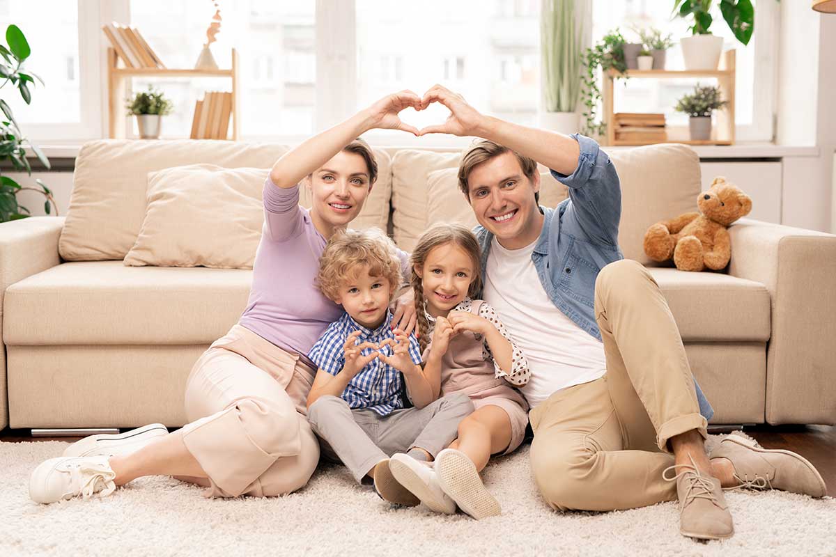 Happy parents and adorable Children sitting on the floor next to the sofa in front of the front camera and making heart shapes with their fingers around Gomlaza Lifestyle Accessories